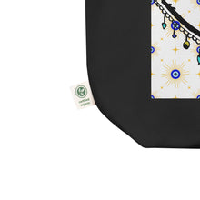 Load image into Gallery viewer, close up image of tag showing certified organic. black colored tote bag with image of eye of protection/evil eye, colors of golden yellow, blue, light blue, third eye, eye, celestial stars. certified organic, cotton.