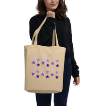 Load image into Gallery viewer, woman modeling/holding oyster colored tote bag, certified organic, features rows of purple stars, with each row darker than the one above it, creating a striking gradient effect. 4 shades of purple.