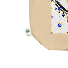 Load image into Gallery viewer, close up image of tag showing certified organic, oyster colored tote bag with image of eye of protection/evil eye, colors of golden yellow, blue, light blue, third eye, eye, celestial stars. certified organic, cotton.