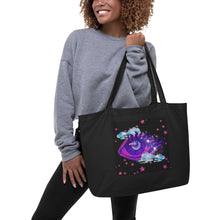 Load image into Gallery viewer, woman holding/modeling large black tote bag, certified organic, tote bag, dreamy eye with a crescent moon in the iris, surrounded by soft, whimsical clouds, pink and purple stars, orange highlights.