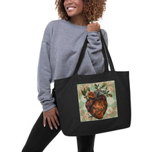 Load image into Gallery viewer, woman modeling/holding large black tote bag, certified organic. Image design: Red illustrated heart with vines and rose, wavy green checkered print background behind the image