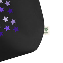 Load image into Gallery viewer, close up image of black tote bag, showing tag certified organic, cotton, features rows of purple stars, with each row darker than the one above it, creating a striking gradient effect. 4 shades of purple.