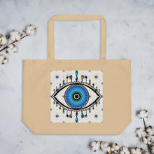 Load image into Gallery viewer, large oyster colored tote bag with image of eye of protection/evil eye, colors of golden yellow, blue, light blue, third eye, eye, celestial stars. certified organic, cotton.