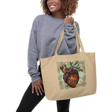 Load image into Gallery viewer, woman modeling/holding large oyster colored tote bag, certified organic. Image design: Red illustrated heart with vines and rose, wavy green checkered print background behind the image