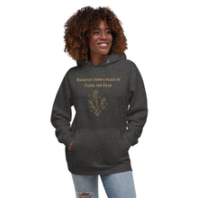 Load image into Gallery viewer, woman modeling/wearing charcoal grey heather unisex hoodie, with pockets, with image phrase: "manifest from a place of faith, not fear." with image graphic of flowers, moon, stardust. Front view.