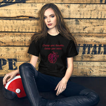 Load image into Gallery viewer, woman modeling/wearing unisex black t-shirt, with image design: red half brain, half heart. Image phrase: Red text - Change your thoughts, change your world. Front view.