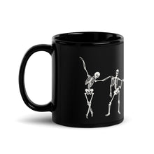 Load image into Gallery viewer, 11 oz. solid black ceramic coffee/tea mug with solid black handle, rim, and inside, outside. Image Design:  
 white minimalist skeletons in line, dancing and posing. Left hand side view. Halloween, spooky season.
