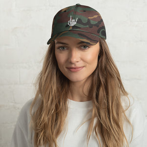 Woman wearing/modeling Camouflage print  Baseball cap, classic visor shape. Image Design: "Rock On" skeleton hand gesture on the front. Front center view.