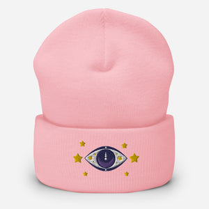 cuffed beanie baby pink, with image design of purple eye of protection/evil eye, with yellow stars. background: winter themed, Christmas gifts.