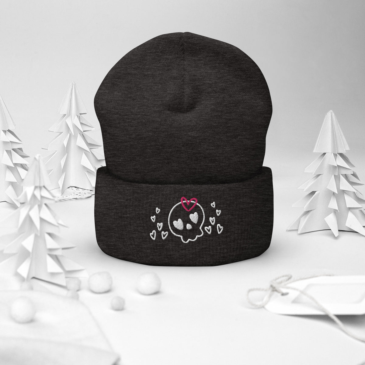 beanie dark grey, with image design of a cartoonish cute skull with heart eyes, a heart bow, and stars. Front view.