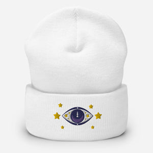 cuffed beanie white, with image design of purple eye of protection/evil eye, with yellow stars. background: winter themed, Christmas gifts.