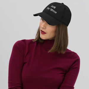 Woman modeling/wearing Black distressed hat. Baseball cap. Phrase: 100% That Witch. Featuring bold embroidered white lettering on the front, playful and stylish. Left side view.