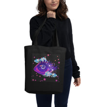 Load image into Gallery viewer, woman holding/modeling black tote bag, certified organic, tote bag, dreamy eye with a crescent moon in the iris, surrounded by soft, whimsical clouds, pink and purple stars, orange highlights.
