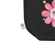 Load image into Gallery viewer, black tote bag, close up image of tag showing certified organic, watercolor daisies with skull faces at their centers, mix of cute and creepy-cute, purple daisy, orange daisy, fuchsia pink daisy, black daisy. adorned with cute yellow stars.
