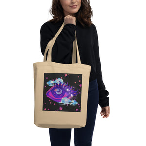 woman holding/modeling oyster beige tote bag, certified organic, tote bag, dreamy eye with a crescent moon in the iris, surrounded by soft, whimsical clouds, pink and purple stars, orange highlights.