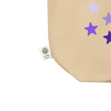 Load image into Gallery viewer, close up image of oyster colored tote bag, showing tag certified organic, cotton, features rows of purple stars, with each row darker than the one above it, creating a striking gradient effect. 4 shades of purple.
