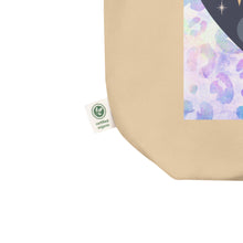 Load image into Gallery viewer, close up of tag, showing certified organic, oyster colored tote bag, certified organic. Image design: blue mystical heart with eye in middle, and crescent moons, and a light purple leopard print background behind the image
