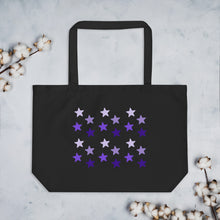 Load image into Gallery viewer, black tote bag, certified organic, cotton, features rows of purple stars, with each row darker than the one above it, creating a striking gradient effect. 4 shades of purple. 
