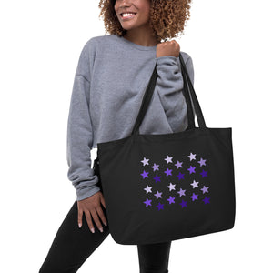 woman modeling/holding black tote bag, certified organic, features rows of purple stars, with each row darker than the one above it, creating a striking gradient effect. 4 shades of purple.