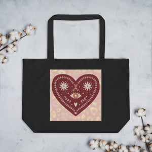 large black tote bag, certified organic. Image design: boho warm red mystical heart with eye in middle, and daisies, and a light red-gold leopard print background behind the image