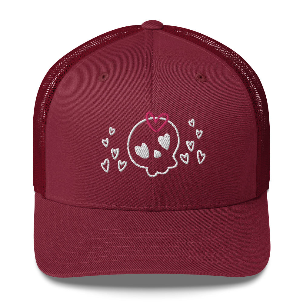 retro trucker hat/cap cranberry red, with image design of a cartoonish cute skull with heart eyes, a heart bow, and stars. Front view.