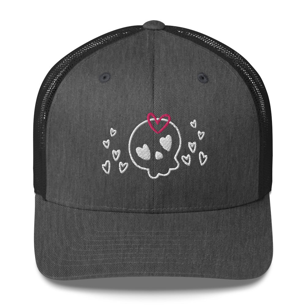 retro trucker hat/cap dark grey heather, with image design of a cartoonish cute skull with heart eyes, a heart bow, and stars. Front view.