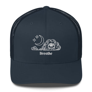 retro trucker hat/cap navy blue , with image design of an eye in a cloud, with moon crescent and stars, with the word "Breathe" underneath the image.  Front view.