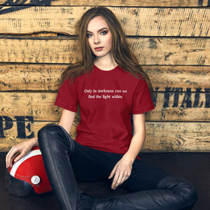 woman modeling/wearing unisex cardinal red t-shirt, with image phrase: "only in darkness can we find the light within." Front view.