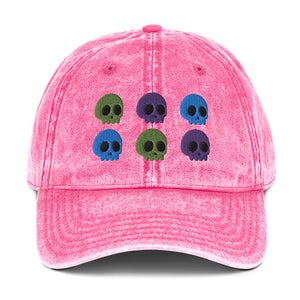 vintage denim cap pink, with image design of 6 purple, green, and blue skulls, 2 of each color, in two rows.  Front view.