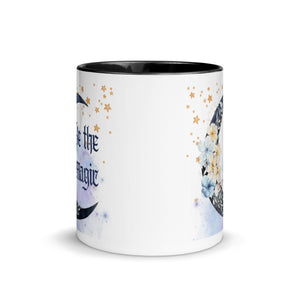 11 oz. white ceramic coffee/tea mug with solid black handle, rim, and inside. Image Design: watercolor blue crescent moon, with flowers, daisies, lilies, butterflies. Stars in background, smoky purple background. Image phrase: Be the Magic. Center front view. Halloween, spooky season.