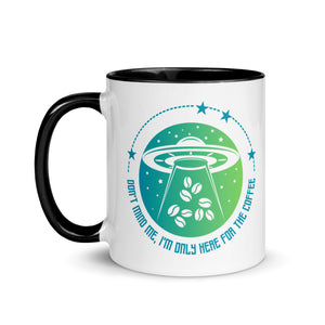 11 oz. white ceramic coffee/tea mug with solid black  handle, rim, and inside. Image Design: ufo ship abducting/beaming up coffee beans. background blue to light green gradient, stars. Text under image: "Don't mind me, I'm only here for the Coffee." left hand side view.