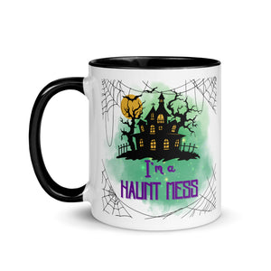 11 oz. white ceramic coffee/tea mug with solid black handle, rim, and inside. Image Design: a silhouette of a haunted house, with a moon behind it, and cosmic green cloud behind image. Spider webs in each corners of image. Image phrase: I'm a Haunt Mess. Left hand side view. Halloween, spooky season.