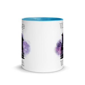 11 oz. white ceramic coffee/tea mug with solid light blue handle, rim, and inside. Image Design: silhouette of black haunted house, cosmic purple cloud in background. Image phrase: Village witch. Center front view. Halloween, spooky season.