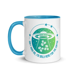 11 oz. white ceramic coffee/tea mug with solid light blue handle, rim, and inside. Image Design: ufo ship abducting/beaming up coffee beans. background blue to light green gradient, stars. Text under image: "Don't mind me, I'm only here for the Coffee." left hand side view.