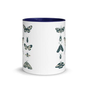 11 oz. white ceramic coffee/tea mug with solid navy blue handle, rim, and inside. Image Design:  vintage beige and blue print images of various moths, butterflies, and beetles, all arranged in rows and columns. Center front view. Halloween, spooky season.