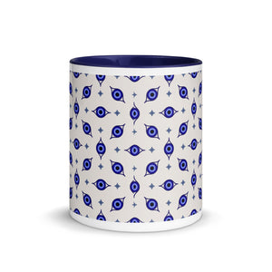 11 oz. white ceramic  coffee/tea mug with solid navy blue handle, rim, and inside. Wrapped around mug is patterned image of eye of protection/evil eye. Outside middle view.