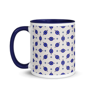 11 oz. white ceramic coffee/tea mug with solid navy blue handle, rim, and inside. Wrapped around mug is patterned image of eye of protection/evil eye. Left hand side view.