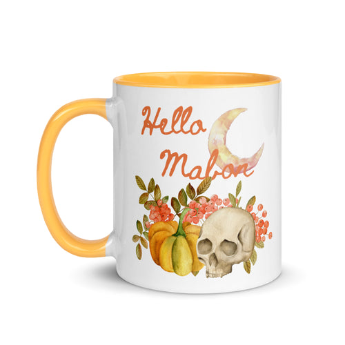 11 oz. white ceramic coffee/tea mug with solid golden yellow handle, rim, and inside. Image Design:  watercolor pumpkin, and skull, leaves and berries behind. Crescent moon in background. Image phrase: Hello Mabon. Left hand side view. Halloween, spooky season.