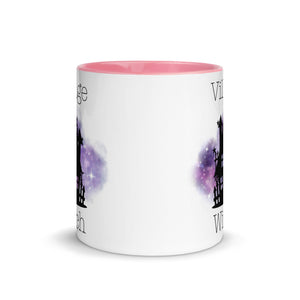 11 oz. white ceramic coffee/tea mug with solid light pink handle, rim, and inside. Image Design: silhouette of black haunted house, cosmic purple cloud in background. Image phrase: Village witch. Center front view. Halloween, spooky season.