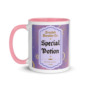 11 oz. white ceramic coffee/tea mug with solid light pink handle, rim, and inside. Image Design: potion label that says 'Special Potion' with brand name above 'Dreaded Banshee Co., established 1690.' Purple-bluish background color with motif of suns, crescent moons, stars, constellations. Image phrase: Special Potion. Left hand side view. Halloween, spooky season.