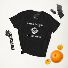 Load image into Gallery viewer, Woman&#39;s black t-shirt with image phrase: thick thighs, witch vibes. Witch&#39;s knot, with crescent moons, and star in the middle. Front view. Halloween, spooky season.
