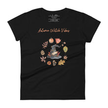 Load image into Gallery viewer, Woman&#39;s black t-shirt with image phrase in light orange font: Autumn Witch Vibes, with image of picturebook witch hat adorned with brown vines, autumn leaves, red-orange berries. A circle of leaves, acorns, pinecone, daisy flower, and mushroom, encircled the hat. Front view. Halloween, spooky season.
