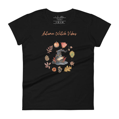 Woman's black t-shirt with image phrase in light orange font: Autumn Witch Vibes, with image of picturebook witch hat adorned with brown vines, autumn leaves, red-orange berries. A circle of leaves, acorns, pinecone, daisy flower, and mushroom, encircled the hat. Front view. Halloween, spooky season.