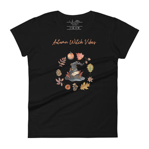 Woman's black t-shirt with image phrase in light orange font: Autumn Witch Vibes, with image of picturebook witch hat adorned with brown vines, autumn leaves, red-orange berries. A circle of leaves, acorns, pinecone, daisy flower, and mushroom, encircled the hat. Front view. Halloween, spooky season.