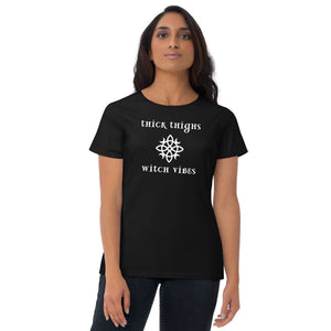 Woman modeling/wearing woman's black t-shirt with image phrase: thick thighs, witch vibes. Witch's knot, with crescent moons, and star in the middle. Front view. Halloween, spooky season.