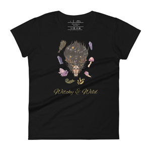 Woman's black t-shirt with image phrase: Witchy & Wild, with image of woman's head with antlers, and stars in her hair. Circling her head are crystals, frog, snail, fern leaf, bunch of flowers, mushroom. Front view. Halloween, spooky season.