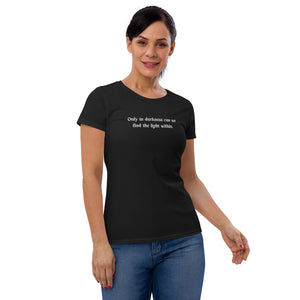 woman modeling/wearing women's black t-shirt, with image phrase: "only in darkness can we find the light within." Front view.