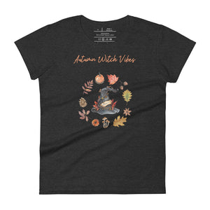 Woman's dark heather grey t-shirt with image phrase in light orange font: Autumn Witch Vibes, with image of picturebook witch hat adorned with brown vines, autumn leaves, red-orange berries. A circle of leaves, acorns, pinecone, daisy flower, and mushroom, encircled the hat. Front view. Halloween, spooky season.