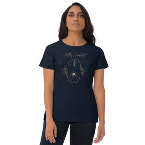 Woman modeling/wearing woman's navy blue t-shirt with image phrase: Witchy Wanderlust. Image under phrase is a minimalist hill with a sun behind, stars in the sky, and crystal suspended above the hill. Bordered with crescent moon on either side. Front view. Halloween, spooky season.