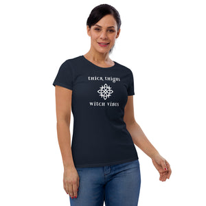 Woman modeling/wearing woman's navy blue t-shirt with image phrase: thick thighs, witch vibes. Witch's knot, with crescent moons, and star in the middle. Front view. Halloween, spooky season.